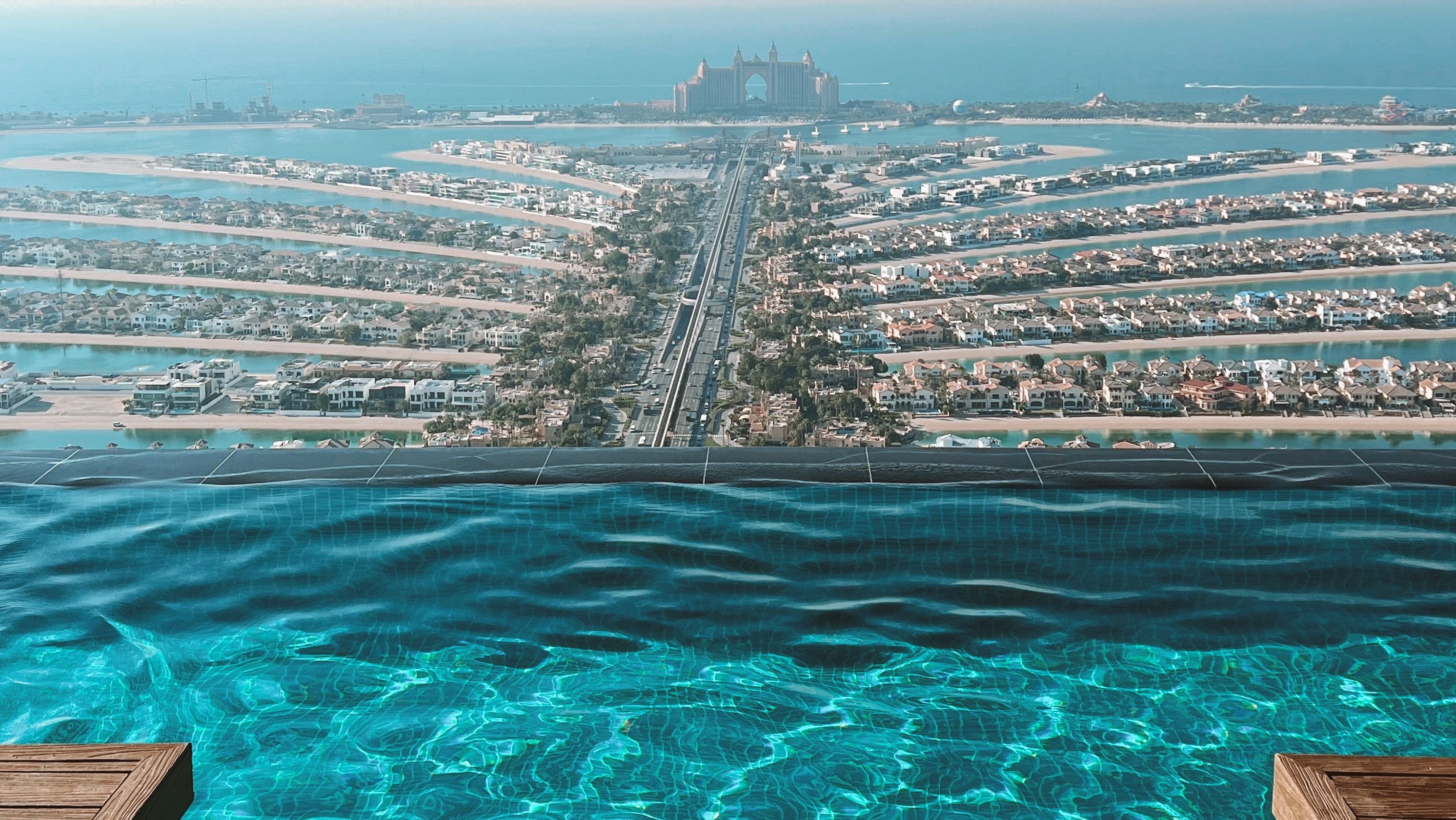 The infinity edge of a rooftop pool on Palm Jumeirah, looking down the trunk of the island toward Atlantis on the crescent